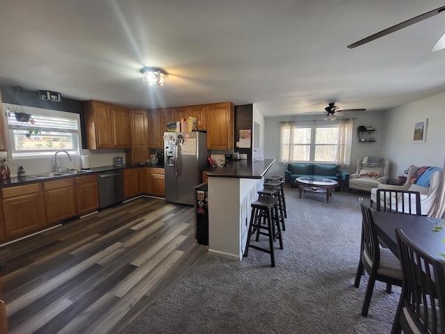 kitchen with brown cabinets, a sink, dark countertops, stainless steel appliances, and a healthy amount of sunlight