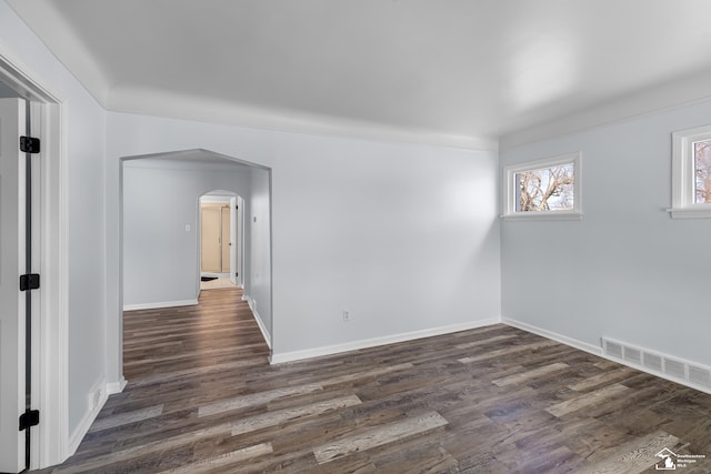 spare room featuring visible vents, arched walkways, baseboards, and dark wood finished floors