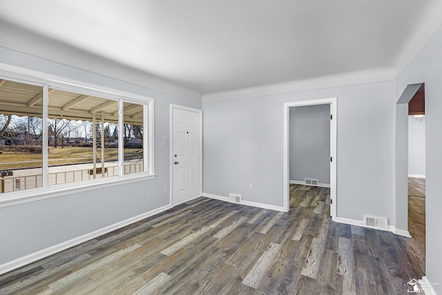 empty room with wood finished floors, visible vents, and baseboards