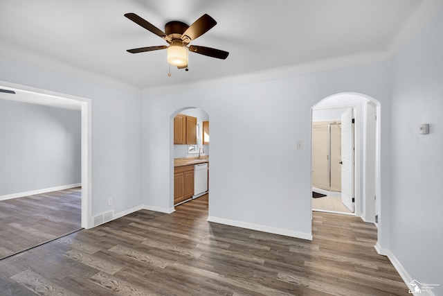 spare room featuring visible vents, a ceiling fan, a sink, dark wood-style floors, and arched walkways