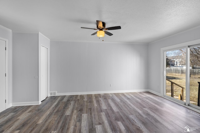 empty room featuring wood finished floors, baseboards, visible vents, a textured ceiling, and crown molding