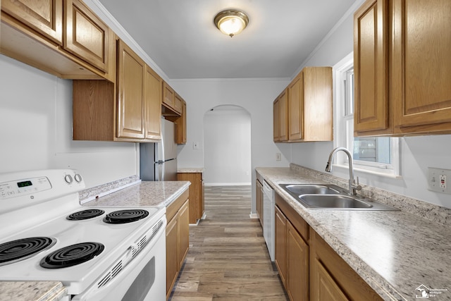 kitchen with light wood finished floors, light countertops, arched walkways, white appliances, and a sink