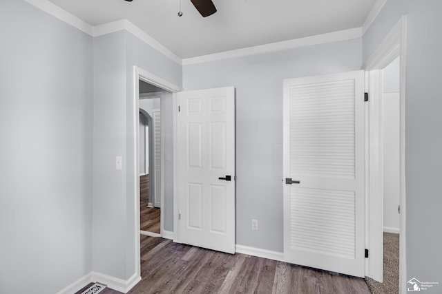 unfurnished bedroom featuring baseboards, ornamental molding, wood finished floors, arched walkways, and a ceiling fan