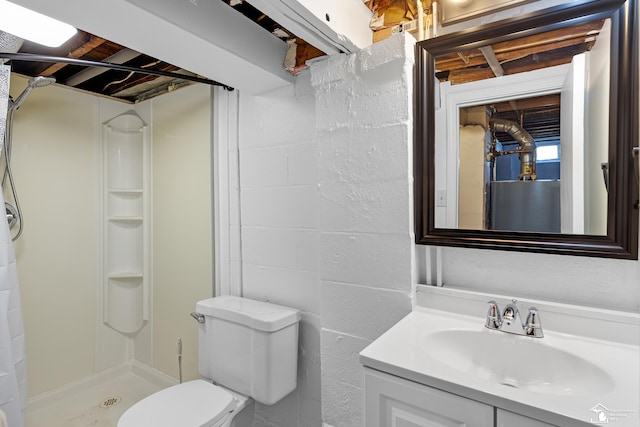 bathroom with concrete block wall, a stall shower, toilet, and vanity