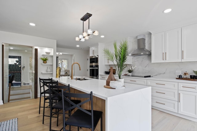 kitchen with a sink, light wood-style floors, appliances with stainless steel finishes, white cabinetry, and wall chimney exhaust hood