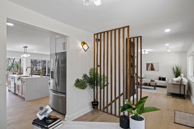 corridor featuring recessed lighting, baseboards, light wood-style floors, and a sink