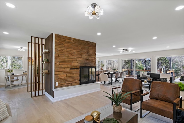 living area with baseboards, light wood finished floors, recessed lighting, a stone fireplace, and a chandelier