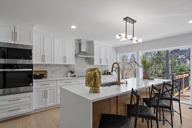 kitchen featuring a sink, stainless steel appliances, light countertops, wall chimney range hood, and backsplash