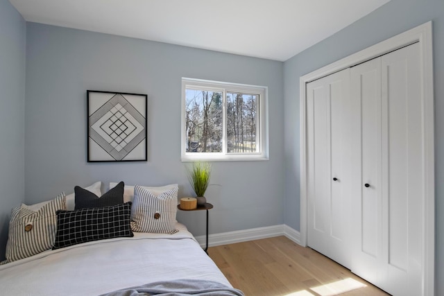 bedroom with a closet, light wood-style flooring, and baseboards