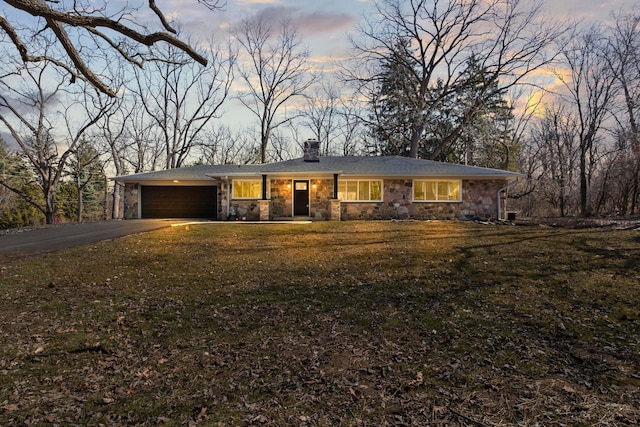 view of front of property with driveway, a front lawn, stone siding, an attached garage, and a chimney