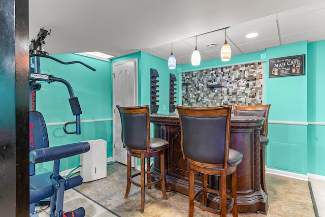 bar with a bar, a paneled ceiling, and baseboards