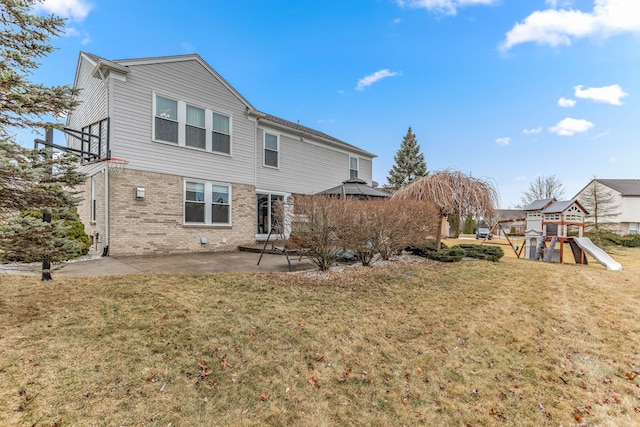 back of house with a patio, brick siding, a lawn, and a playground