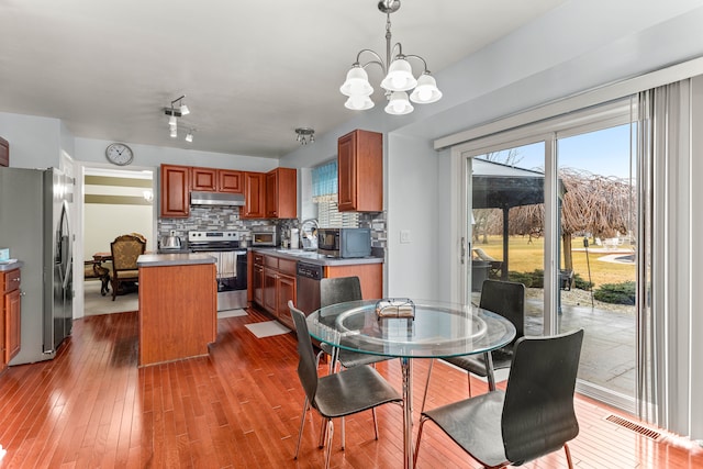 kitchen featuring hardwood / wood-style floors, a kitchen island, under cabinet range hood, appliances with stainless steel finishes, and tasteful backsplash