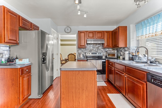 kitchen with a sink, appliances with stainless steel finishes, wood-type flooring, under cabinet range hood, and a center island