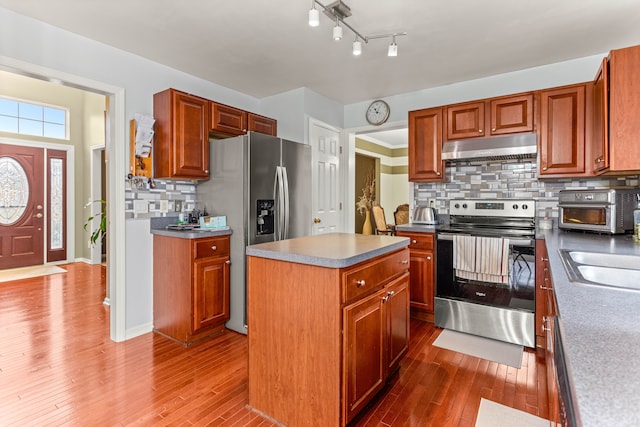 kitchen featuring a kitchen island, under cabinet range hood, decorative backsplash, appliances with stainless steel finishes, and dark wood-style floors