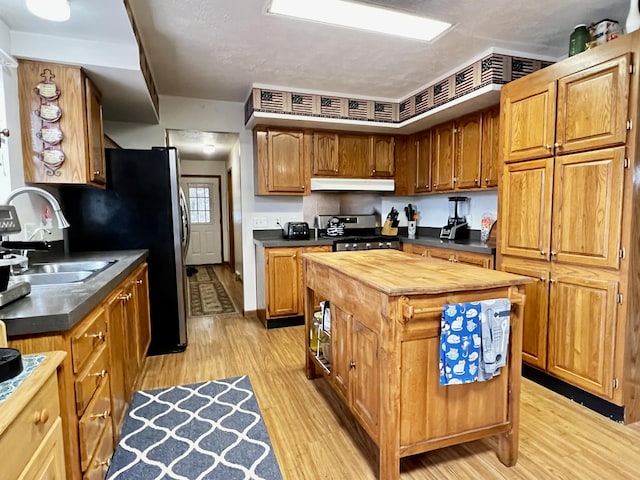 kitchen featuring stainless steel gas range, a sink, butcher block countertops, light wood-style floors, and under cabinet range hood