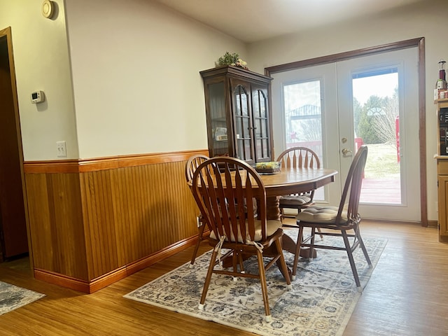 dining space with light wood-type flooring, a wainscoted wall, wood walls, and french doors