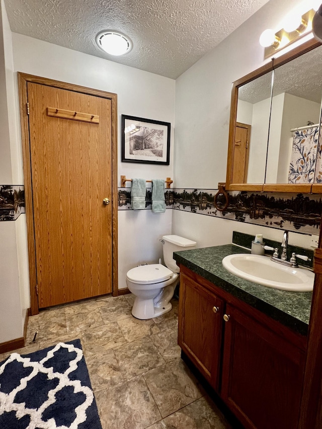 bathroom with toilet, a textured ceiling, vanity, and baseboards