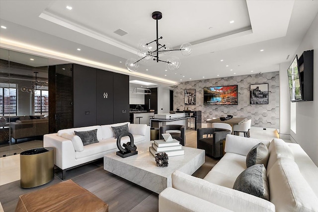 living area featuring visible vents, an accent wall, a tray ceiling, recessed lighting, and an inviting chandelier