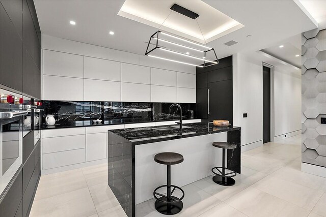 kitchen featuring tasteful backsplash, light tile patterned floors, a kitchen breakfast bar, white cabinetry, and modern cabinets