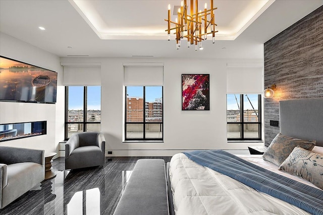 bedroom with a glass covered fireplace, an accent wall, a tray ceiling, and wood finished floors