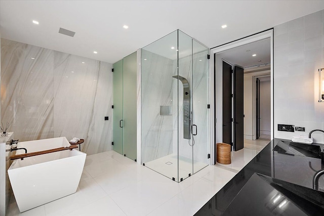 bathroom with a shower stall, recessed lighting, a freestanding tub, tile walls, and a sink