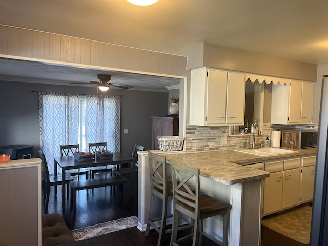 kitchen with decorative backsplash, stainless steel microwave, light countertops, white cabinetry, and a sink