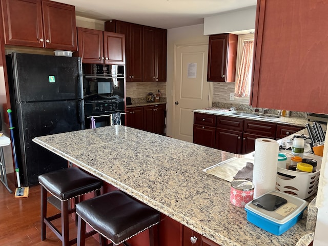 kitchen with black appliances, wood finished floors, tasteful backsplash, and a sink