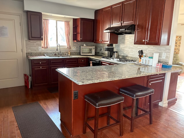 kitchen featuring under cabinet range hood, dark wood-style floors, dark brown cabinets, and a sink