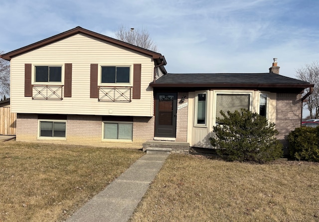 tri-level home featuring brick siding, a chimney, a front lawn, and a shingled roof