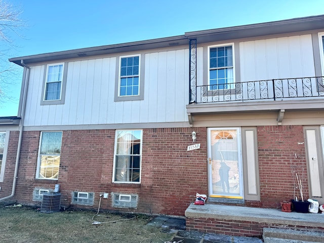 view of front of home with brick siding, a balcony, and central AC unit