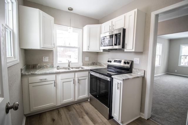 kitchen featuring stainless steel appliances, light countertops, white cabinets, a sink, and baseboards