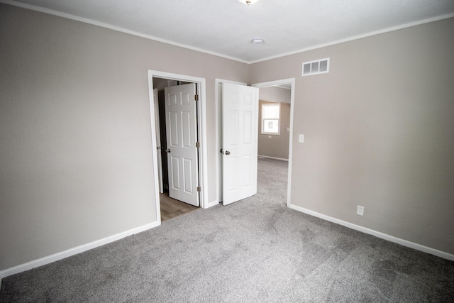 unfurnished bedroom with crown molding, carpet flooring, visible vents, and baseboards