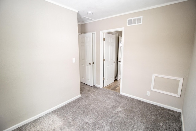 unfurnished bedroom featuring crown molding, visible vents, attic access, carpet flooring, and baseboards