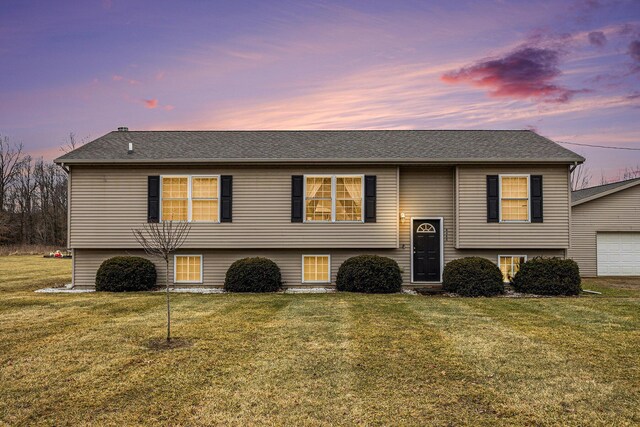 raised ranch with a yard, a garage, and a shingled roof