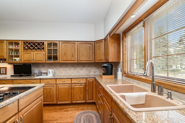 kitchen with brown cabinetry, glass insert cabinets, a sink, and light wood-style flooring