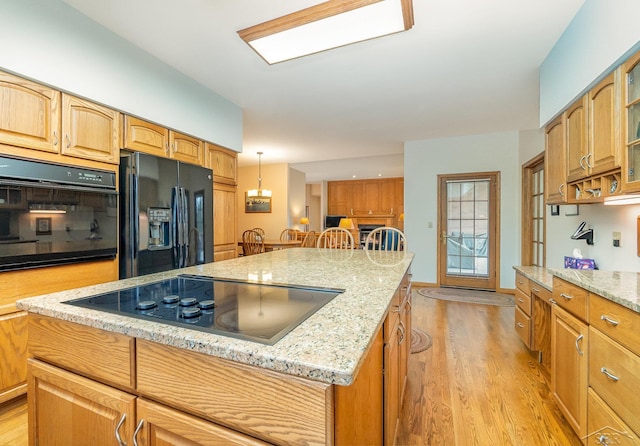 kitchen with light stone countertops, black appliances, light wood-style flooring, and a kitchen island