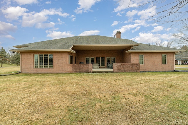 back of house with brick siding, a lawn, and a chimney