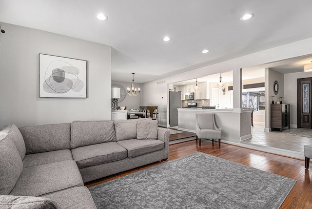 living area with recessed lighting, baseboards, an inviting chandelier, and wood-type flooring