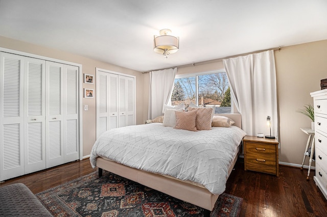 bedroom with dark wood finished floors, baseboards, and two closets