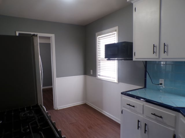 kitchen with white cabinets, tile countertops, wood finished floors, freestanding refrigerator, and black microwave