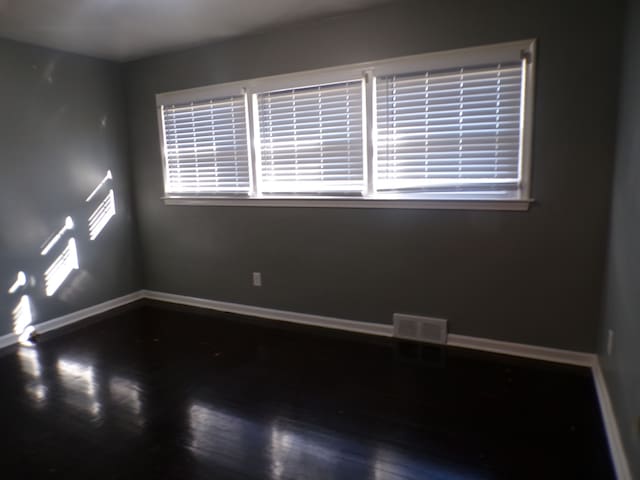 unfurnished room featuring visible vents, baseboards, and wood finished floors