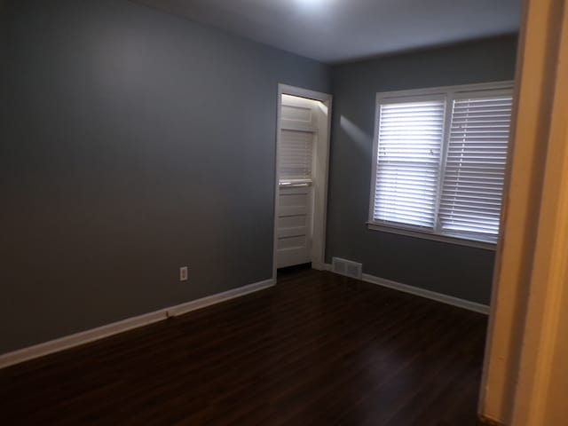 spare room featuring dark wood-type flooring, visible vents, and baseboards