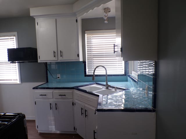 kitchen featuring tile counters, white cabinets, plenty of natural light, and a sink