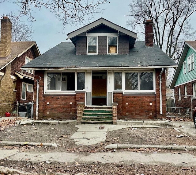 bungalow-style house featuring entry steps, a chimney, fence, and brick siding