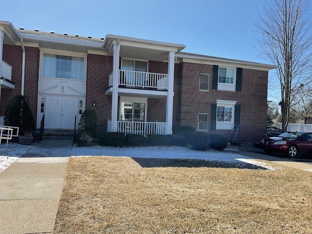 view of front of home with brick siding, a front lawn, a porch, and a balcony