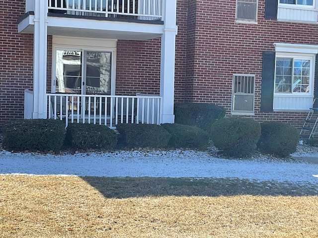 doorway to property featuring covered porch, brick siding, and a balcony