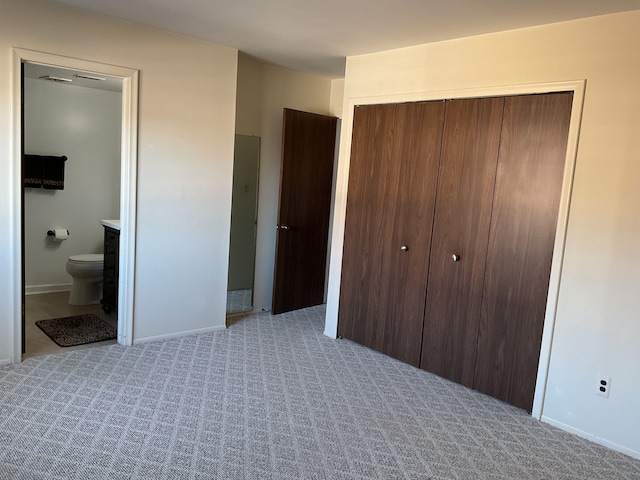 unfurnished bedroom featuring a closet, light colored carpet, baseboards, and ensuite bathroom