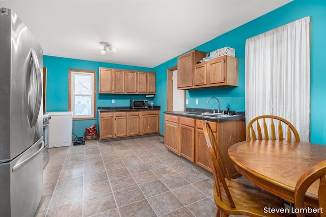 kitchen with stainless steel appliances, dark countertops, a sink, and brown cabinets