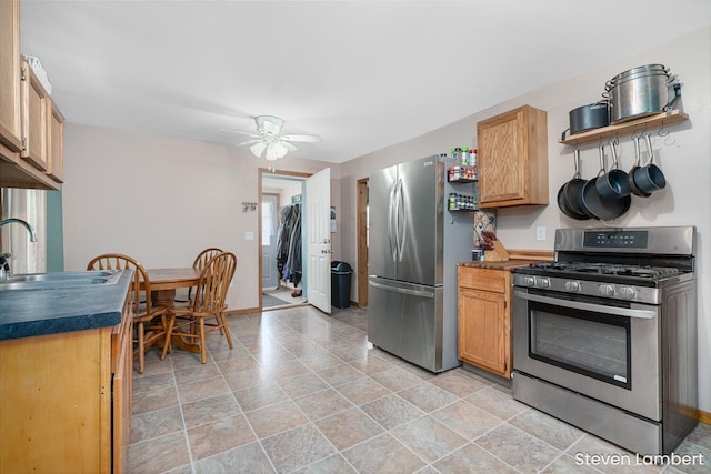 kitchen featuring baseboards, dark countertops, ceiling fan, stainless steel appliances, and a sink